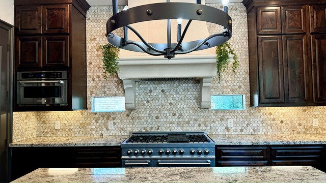 kitchen featuring light stone countertops, dark brown cabinets, backsplash, and stainless steel appliances