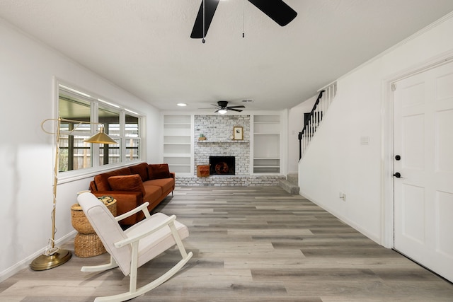 living room with a brick fireplace, a textured ceiling, ceiling fan, built in features, and light hardwood / wood-style floors