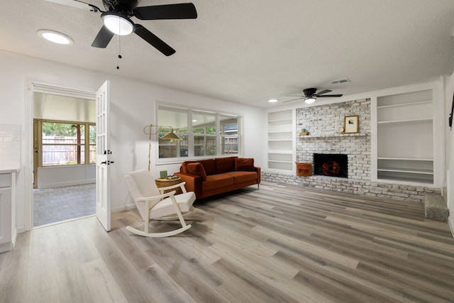 living room featuring a textured ceiling, ceiling fan, light hardwood / wood-style flooring, built in features, and a fireplace