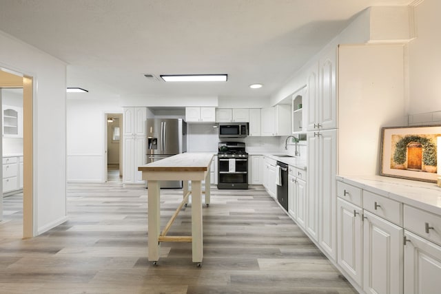 kitchen with sink, light hardwood / wood-style flooring, light stone countertops, appliances with stainless steel finishes, and white cabinetry