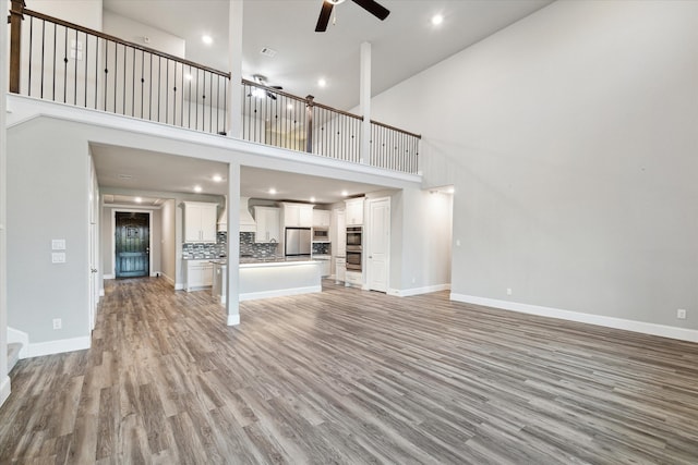 unfurnished living room featuring light hardwood / wood-style floors, ceiling fan, and a high ceiling