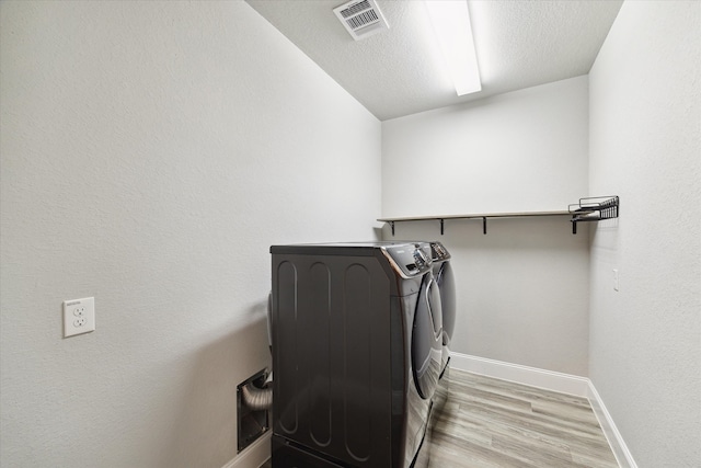 clothes washing area with light wood-type flooring, a textured ceiling, and washer and dryer