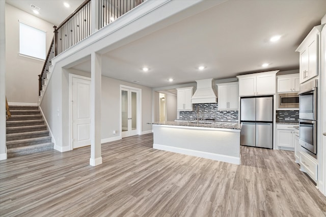 kitchen featuring white cabinetry, custom range hood, appliances with stainless steel finishes, and light hardwood / wood-style flooring