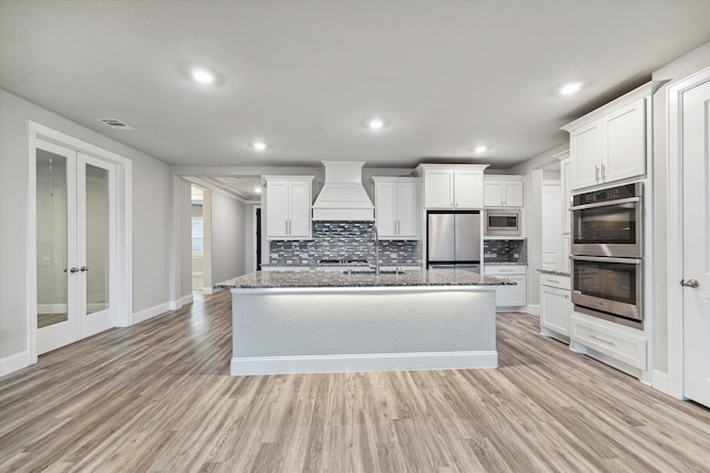 kitchen featuring stainless steel appliances, custom range hood, white cabinetry, and light hardwood / wood-style floors