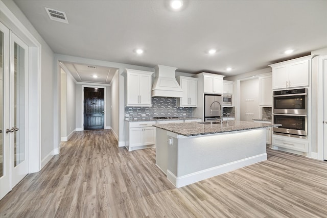 kitchen featuring white cabinetry, appliances with stainless steel finishes, a center island with sink, and custom exhaust hood