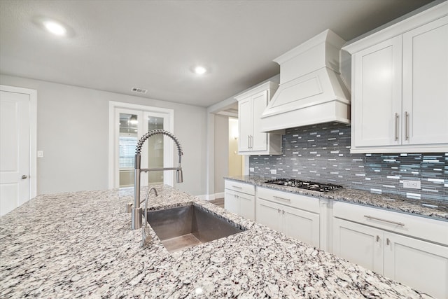 kitchen with white cabinetry, custom range hood, sink, and stainless steel gas cooktop