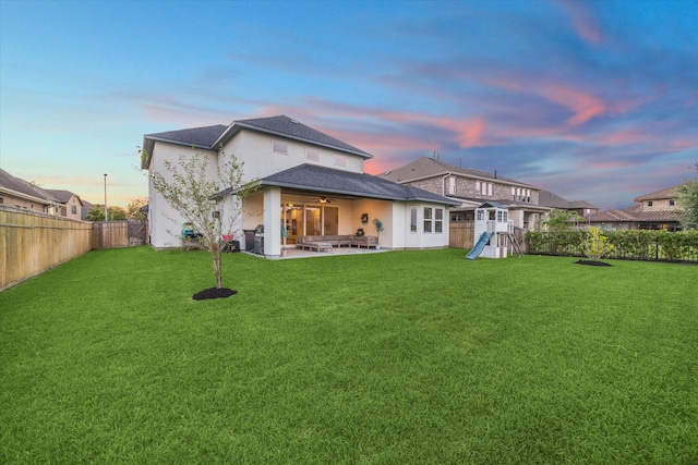 back house at dusk with a patio and a yard