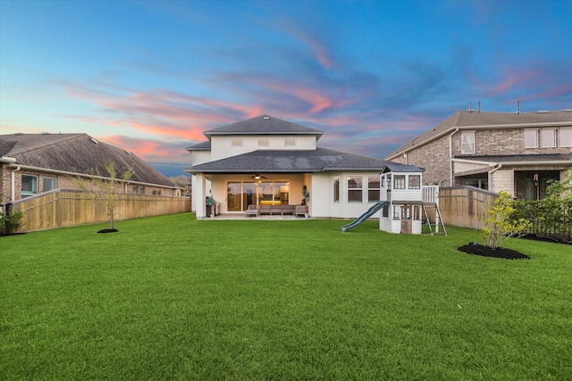 back house at dusk with a patio and a yard