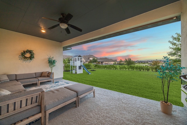 patio terrace at dusk featuring a playground, outdoor lounge area, ceiling fan, and a yard