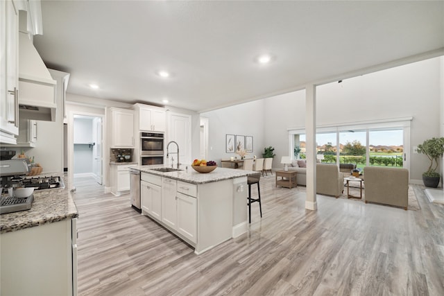 kitchen with white cabinetry, a kitchen island with sink, and light stone counters