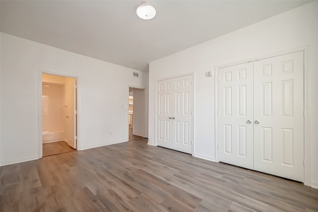 unfurnished bedroom with light hardwood / wood-style floors, two closets, and ensuite bath