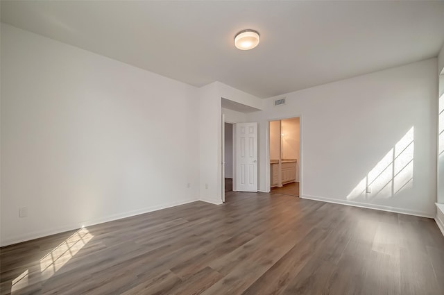 unfurnished bedroom featuring connected bathroom, baseboards, visible vents, and dark wood-style floors