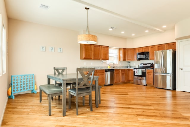 kitchen featuring stainless steel appliances, light wood-type flooring, decorative light fixtures, and sink