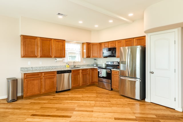 kitchen featuring light stone counters, sink, appliances with stainless steel finishes, and light hardwood / wood-style floors