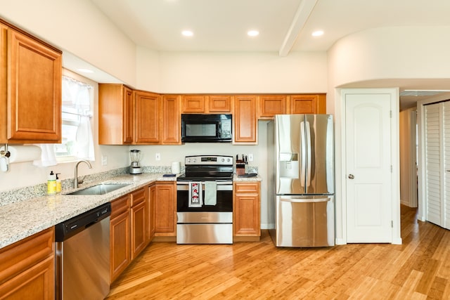 kitchen featuring light stone countertops, appliances with stainless steel finishes, light wood-type flooring, and sink