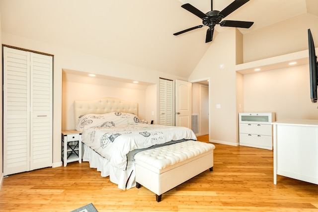 bedroom with high vaulted ceiling, two closets, light hardwood / wood-style floors, and ceiling fan