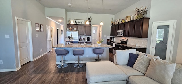 kitchen with appliances with stainless steel finishes, pendant lighting, dark brown cabinetry, a kitchen island with sink, and dark hardwood / wood-style floors