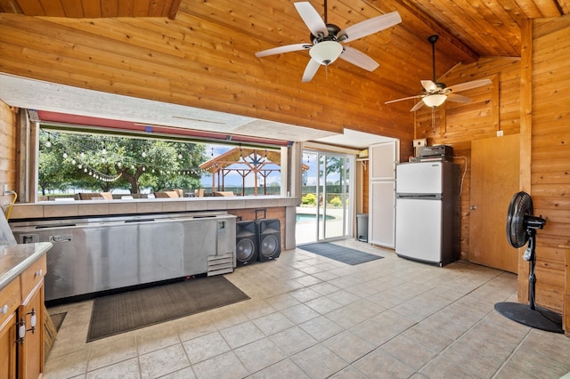 kitchen with wood ceiling, light tile patterned flooring, white fridge, wooden walls, and ceiling fan