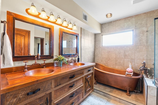 bathroom featuring tile walls, vanity, tile patterned floors, and a washtub