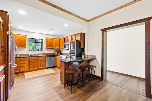 kitchen with appliances with stainless steel finishes, a kitchen bar, light wood-type flooring, and kitchen peninsula