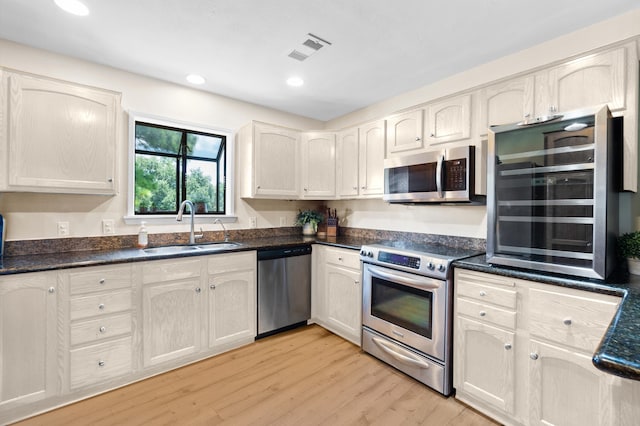 kitchen with appliances with stainless steel finishes, sink, light hardwood / wood-style flooring, and wine cooler