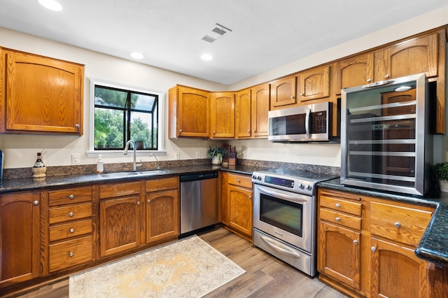 kitchen featuring dark stone counters, light hardwood / wood-style floors, sink, beverage cooler, and appliances with stainless steel finishes