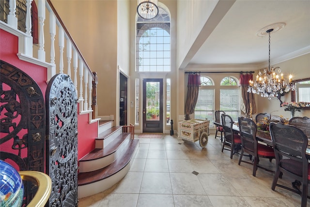 foyer featuring light tile patterned floors, an inviting chandelier, a towering ceiling, and ornamental molding