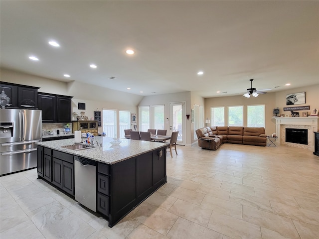 kitchen featuring appliances with stainless steel finishes, light stone counters, a center island, ceiling fan, and sink