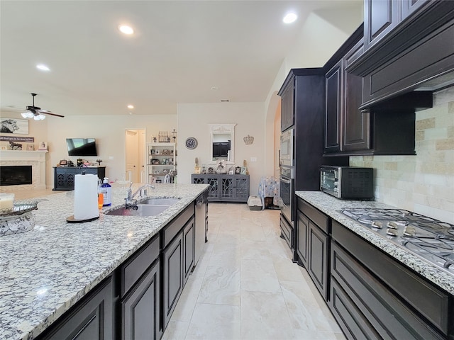 kitchen with ceiling fan, light stone counters, sink, backsplash, and stainless steel appliances