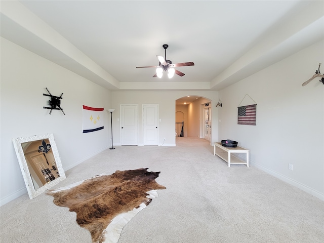 interior space with ceiling fan, a raised ceiling, and light carpet