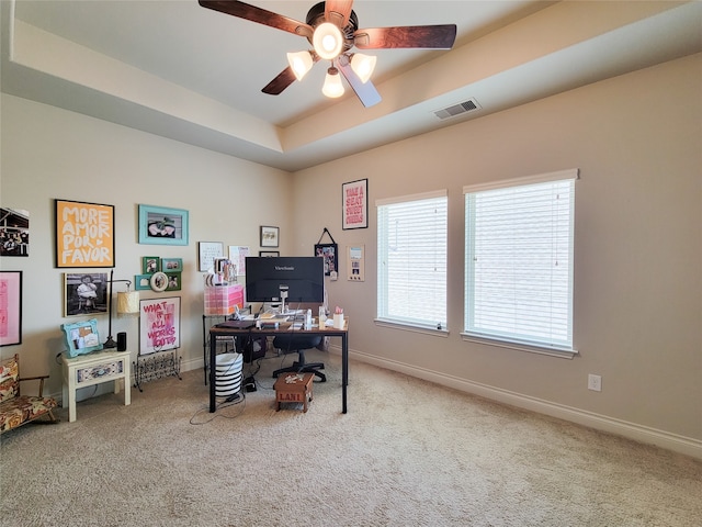 carpeted office with ceiling fan and a raised ceiling