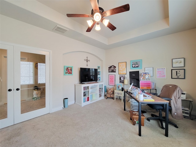 carpeted office space featuring a tray ceiling and ceiling fan