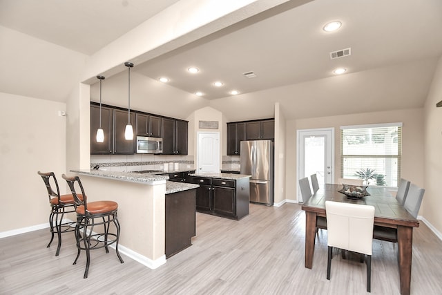 kitchen featuring light hardwood / wood-style floors, kitchen peninsula, stainless steel appliances, lofted ceiling, and decorative light fixtures