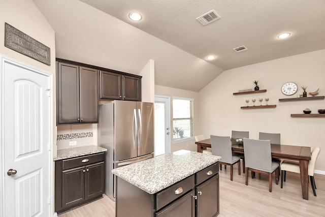 kitchen featuring dark brown cabinets, light stone counters, a center island, lofted ceiling, and light hardwood / wood-style flooring