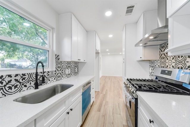 kitchen featuring appliances with stainless steel finishes, white cabinetry, sink, and wall chimney range hood