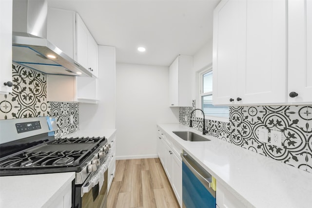 kitchen with light hardwood / wood-style floors, white cabinets, stainless steel appliances, sink, and wall chimney range hood