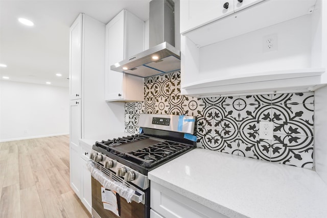 kitchen with wall chimney exhaust hood, stainless steel range with gas cooktop, white cabinetry, and light hardwood / wood-style flooring