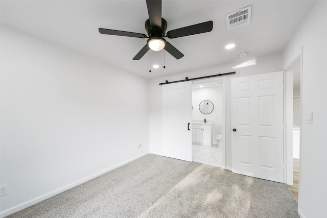 unfurnished bedroom with a barn door, connected bathroom, light carpet, and ceiling fan