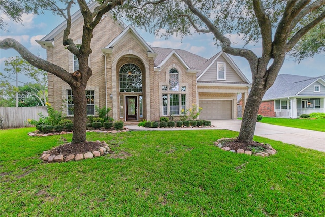 traditional-style house with driveway, fence, a front yard, and brick siding