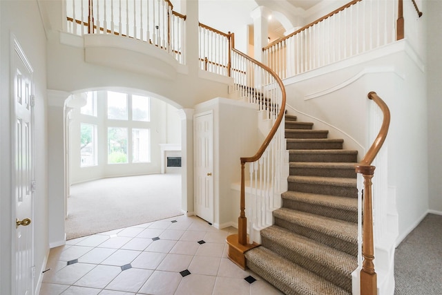 stairway with a high ceiling, a fireplace, baseboards, arched walkways, and carpet floors