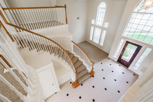 foyer entrance with a high ceiling, tile patterned floors, stairs, and carpet floors