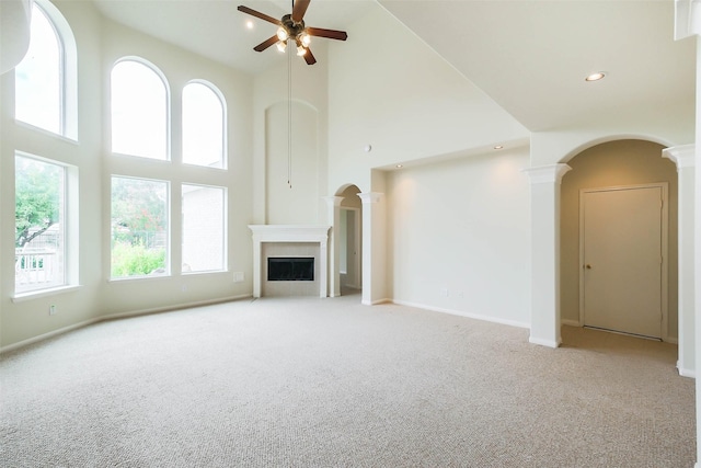 unfurnished living room with carpet flooring, a towering ceiling, ceiling fan, and decorative columns