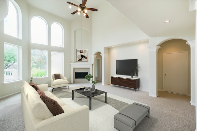 living area with light colored carpet, ceiling fan, a towering ceiling, and decorative columns