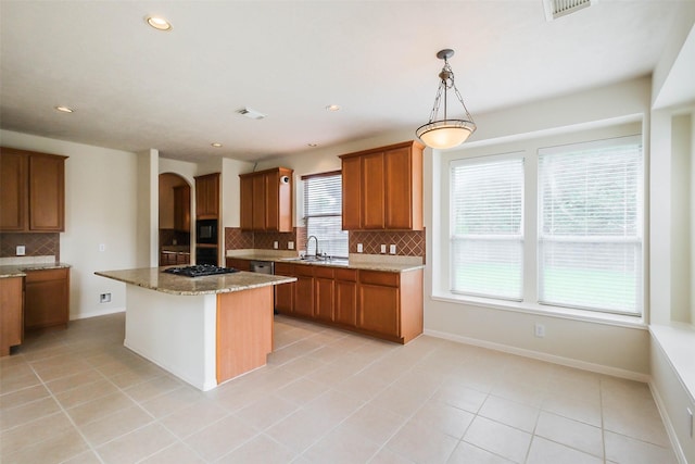 kitchen with arched walkways, light stone counters, brown cabinetry, backsplash, and a center island