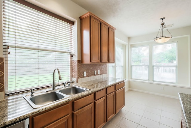 kitchen featuring tasteful backsplash, light tile patterned floors, brown cabinets, a sink, and baseboards