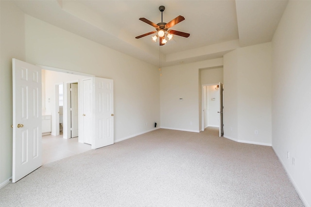 spare room featuring a raised ceiling, ceiling fan, baseboards, and light carpet