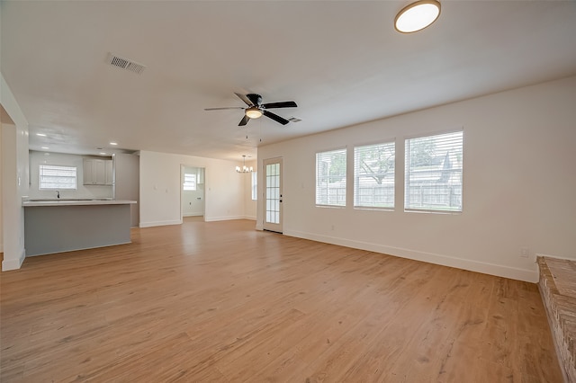 unfurnished living room with ceiling fan with notable chandelier, a healthy amount of sunlight, and light wood-type flooring