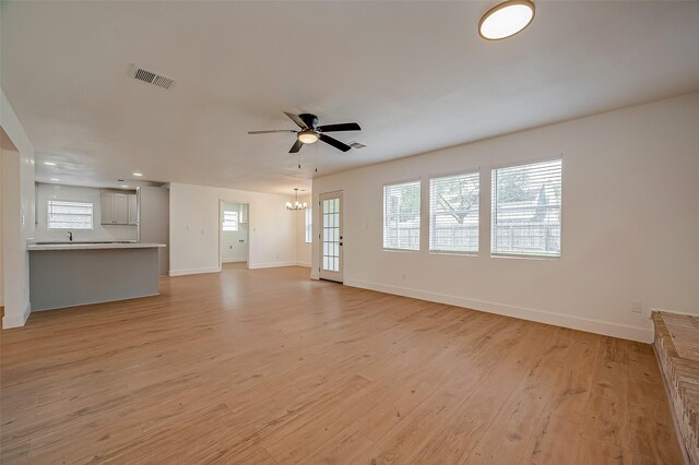 unfurnished living room with ceiling fan with notable chandelier and light hardwood / wood-style floors