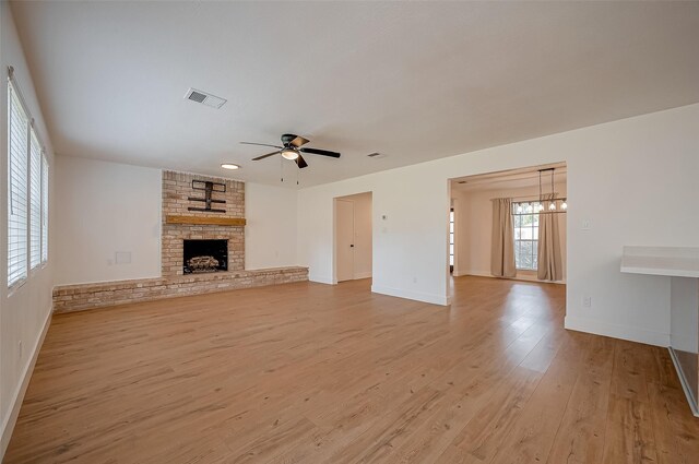 unfurnished living room featuring ceiling fan with notable chandelier, light wood-type flooring, and a fireplace