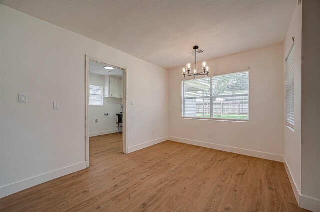 empty room featuring light hardwood / wood-style floors, plenty of natural light, and a notable chandelier